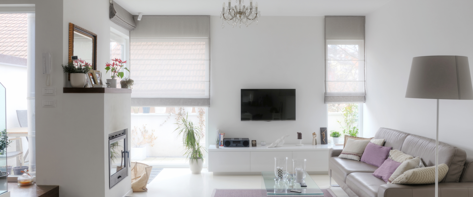 Modern living room with a couch, flat screen television, fireplace and Somfy powered roman shades over the windows.