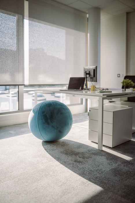 Roller shades lowering in a commercial office with a ball seat and desk in the foreground.